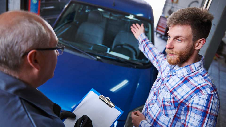 Ein Arbeiter mit Handschuhen und Schürze bearbeitet mit Werkzeugen eine schwarze Recyclingbatterie, umgeben von grünen Recyclingbehältern und umweltfreundlichen Schildern.